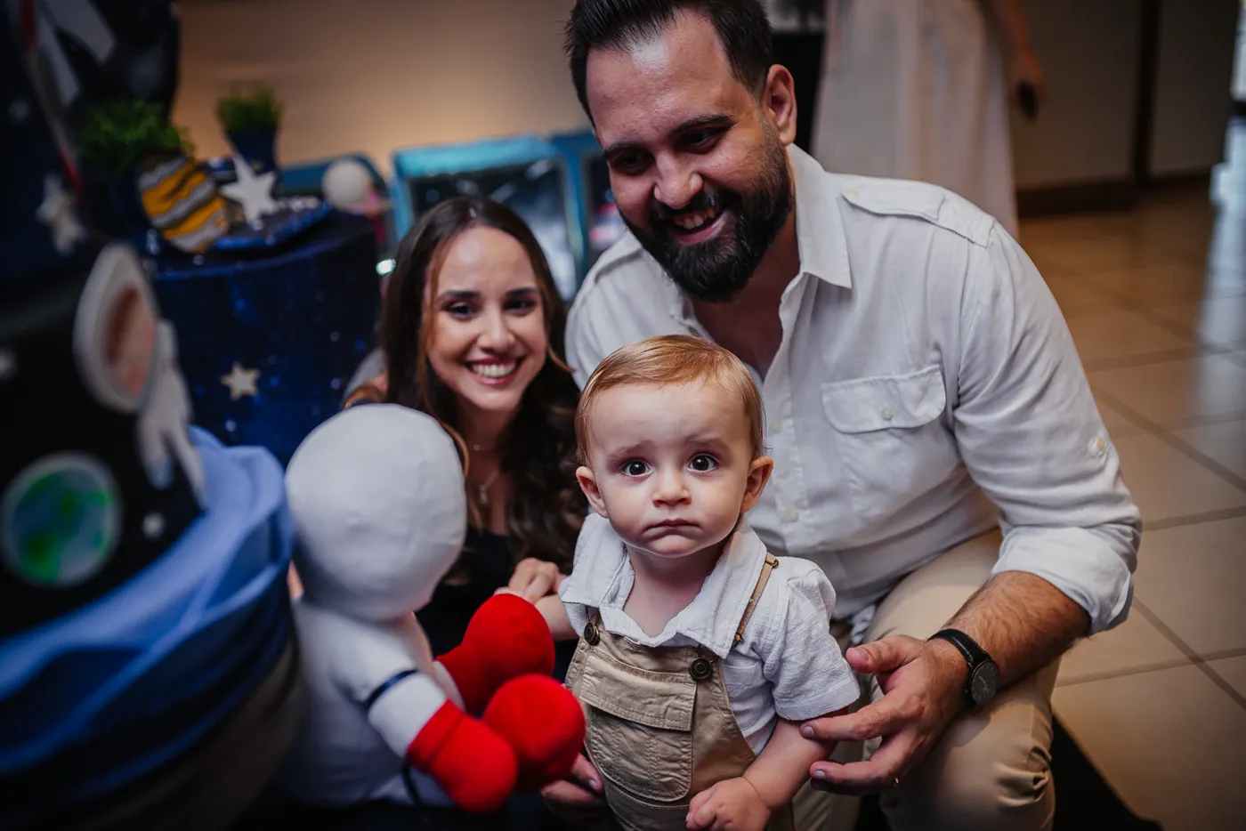 Warlen Miiller sorrindo ao lado da esposa, Carol, e do filho, Enrico, em uma festa de aniversário com tema espacial